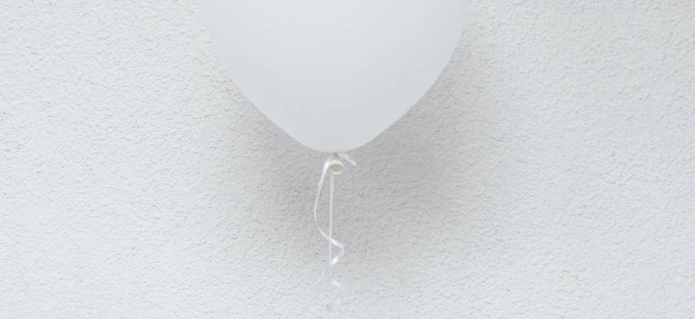 Hand hält weißen Luftballon.