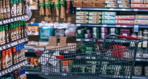 Ein Einkaufswagen steht leer zwischen vollen Supermarktregalen