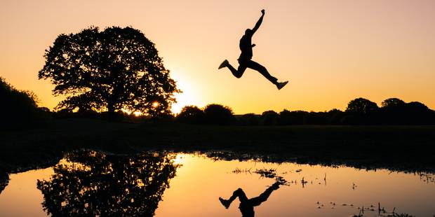 Person springt über Fluss im Abendrot