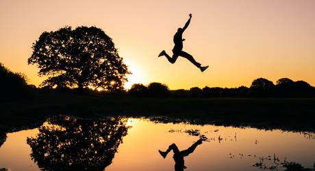 Person springt über Fluss im Abendrot