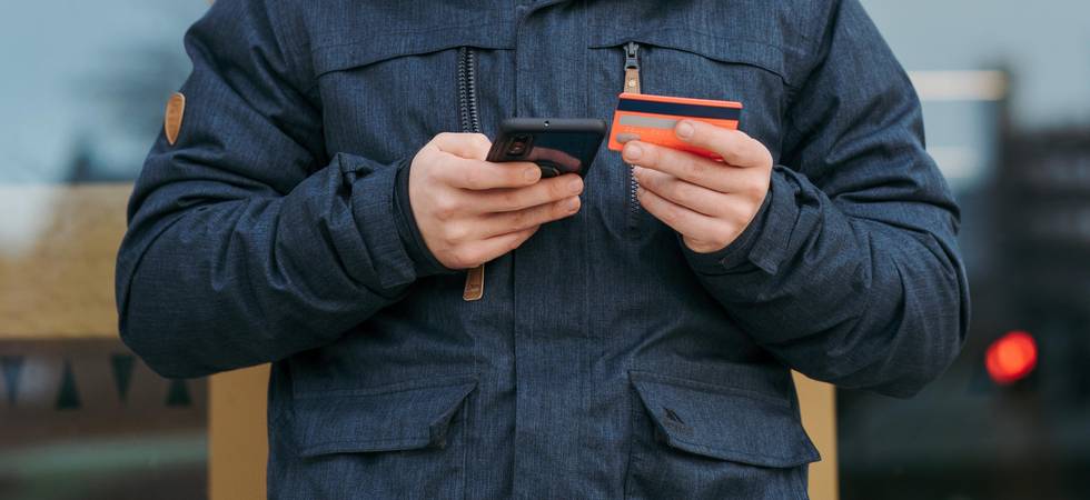 Mann In Schwarzer Strickmütze Und Schwarzer Jacke, der Schwarzes Smartphone und Bankkarte hält
