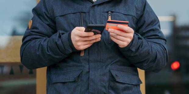 Mann In Schwarzer Strickmütze Und Schwarzer Jacke, der Schwarzes Smartphone und Bankkarte hält
