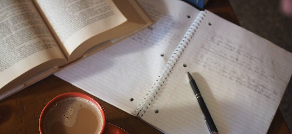 aufgeschlagenes Buch, Block mit Notizen und Bleistift und eine Kaffeetasse auf einem Holztisch