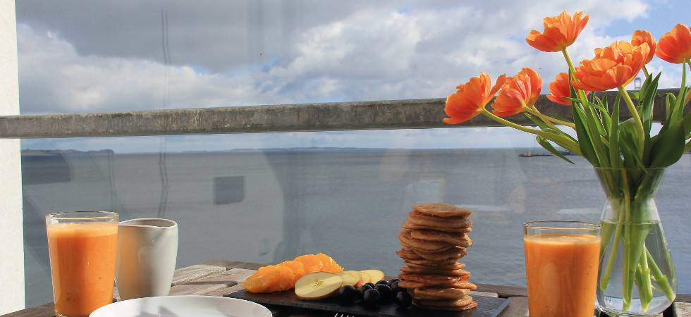 orangene Blumen, Orangensaft und Kekse vor einem Blick aufs Meer