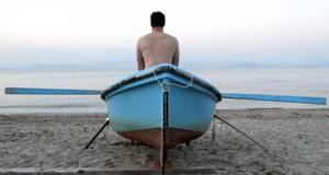 Mann sitzt oberkörperfrei im Boot am Strand