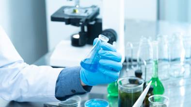 Labor, Mensch in Kittel und blauen Handschuhen hält Reagenzglas mit blauer Flüssigkeit in Hand