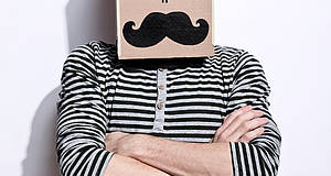 Mann mit gestreiftem Pullover trägt Karton auf dem Kopf mit aufgemaltem Gesicht