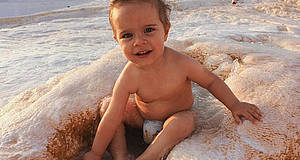 Baby sitzt in Windel im Sand
