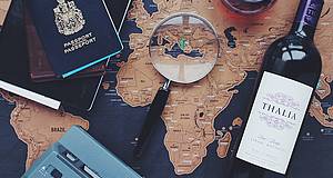 Reisepass, Wein, Lupe liegen auf Weltkarte