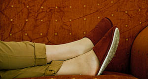 Füße liegen in roten Pantoffeln auf rotem Sofa