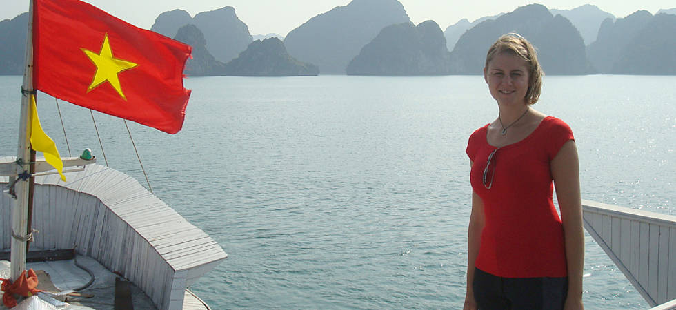 Mädchen auf Boot mit vietnamesischer Flagge, im Hintergrund Wasser und Berge