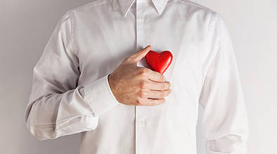 Mann im weißen Hemd hält sich Herz aus Holz vor die Brust