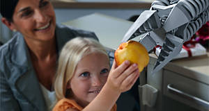 Frau mit Mädchen die einen Roboter mit Apfel füttern