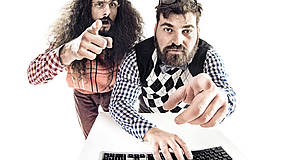 Zwei Männer vor Tastatur mit ausgestreckten Zeigefinger