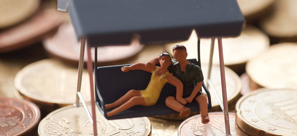 Plastikpuppen als Ehepaar sitzen in Hängeschaukel auf vielen gehäuften Geldmünzen