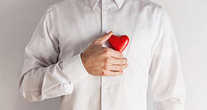 Mann im weißen Hemd hält sich Herz aus Holz vor die Brust