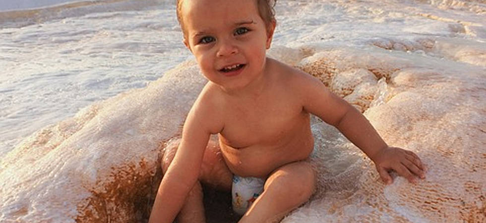 Baby sitzt in Windel im Sand