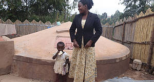 Afrikanische Frau mit Kind vor Lehmhütte