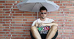 Mann sitzt mit Sonnenbrille und Schirm am Boden