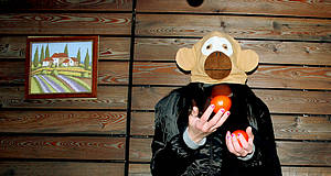 Mann mit Affenmaske jongliert Äpfel