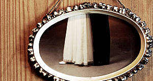 Spiegel hängt an Wand mit Unterteil eines Kleides und Anzuges im Bild