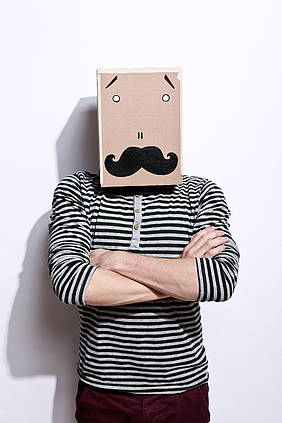 Mann mit gestreiftem Pullover trägt Karton auf dem Kopf mit aufgemaltem Gesicht