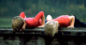 zwei Jungen liegen auf einem Steg und schauen mit den Köpfen nach unten