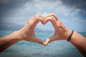 Hände formen ein Herz vor Meer