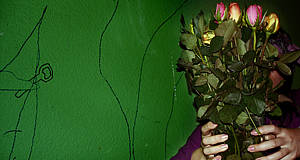 Frau vor grüner Wand hält sich ein Strauß Rosen vors Gesicht