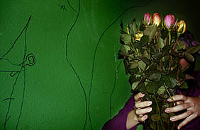 Frau vor grüner Wand hält sich ein Strauß Rosen vors Gesicht