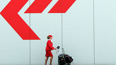 Flugbegleiterin mit Gepäck vor weißer Wand mit rotem Pfeil