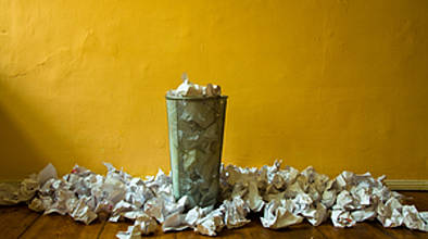 Überfüllter Papierkorb mit Papier auf dem Boden rundum vor gelber Wand