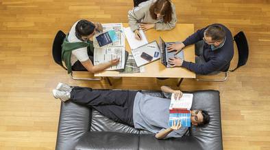 Vier Studierende sitzen an einem Tisch und lernen mit Büchern und Laptop.